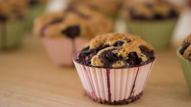 A blueberry muffin in a paper case with more muffins behind it
