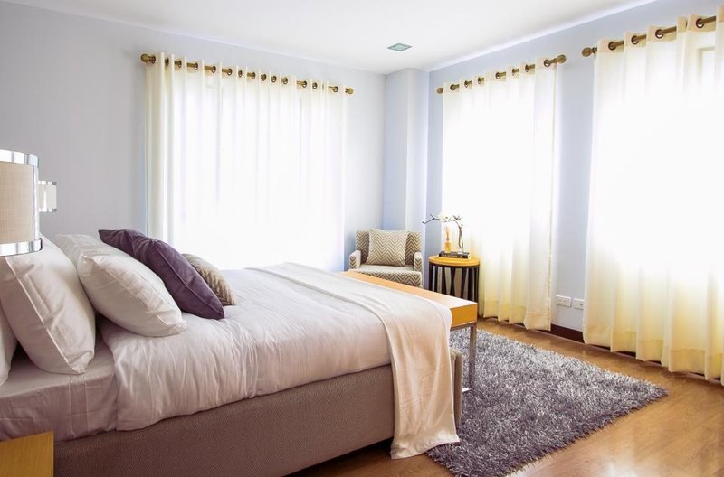 An empty bed with cushions and a folded blanket in a sunlit bedroom