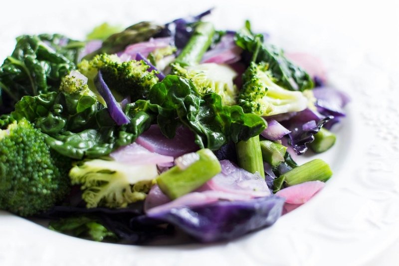 Cooked green vegetables and red onion on a white plate
