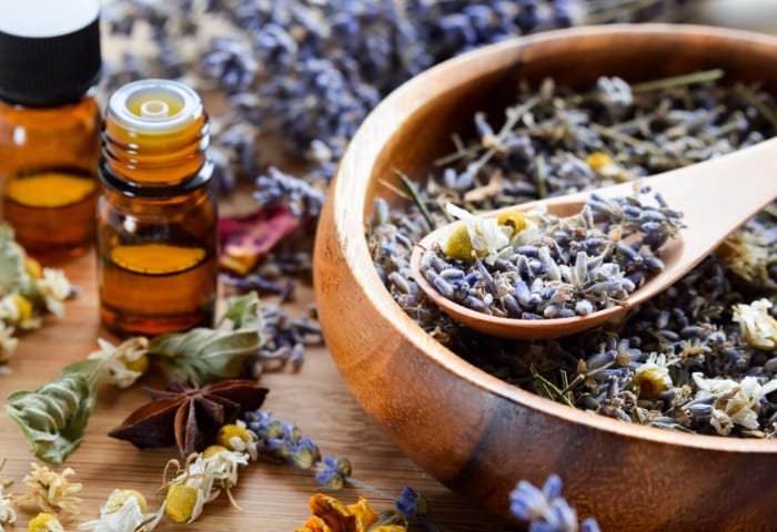 Dried herbs in a bowl beside small bottles