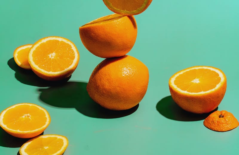 Fresh oranges and orange slices on a green background