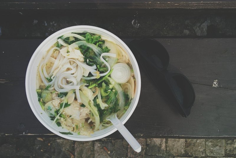 A bowl of chicken noodle soup with fresh herbs and a spoon on a wooden table