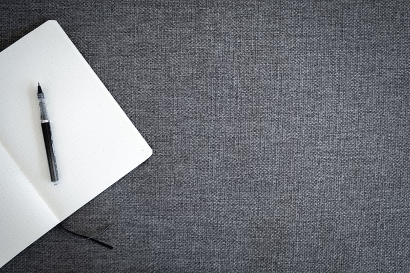 A blank dotted notebook and pen on grey woven fabric