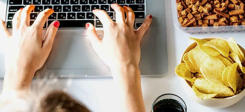A person using a laptop beside snack foods