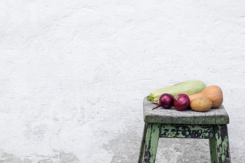 Pumpkins and red onions on a small stool against a pale wall