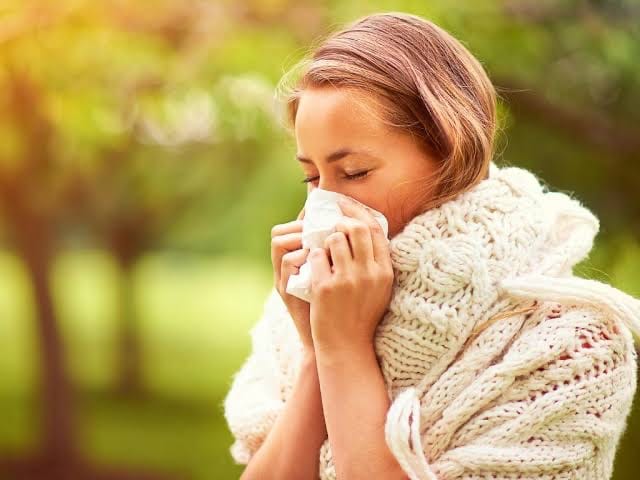 A person wearing a scarf and holding a tissue to their nose outdoors