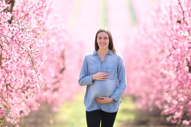 A pregnant woman standing among pink blossoms