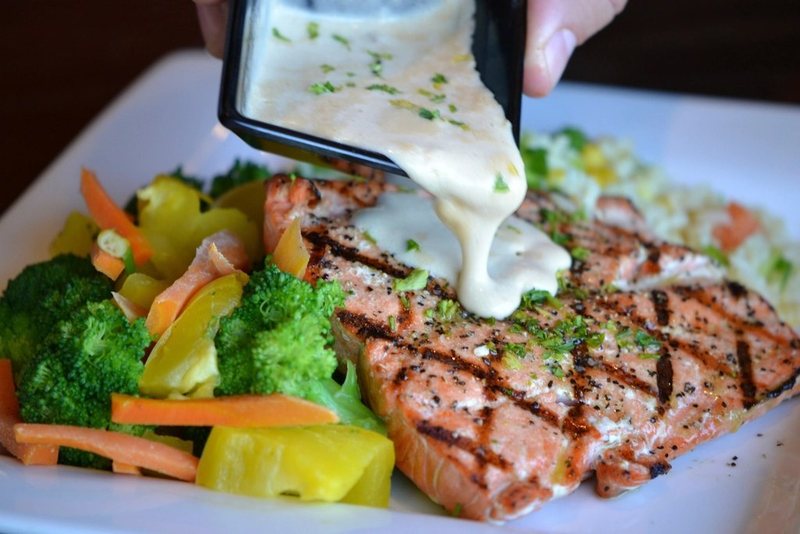A plate of cooked salmon and vegetables with sauce being poured over it