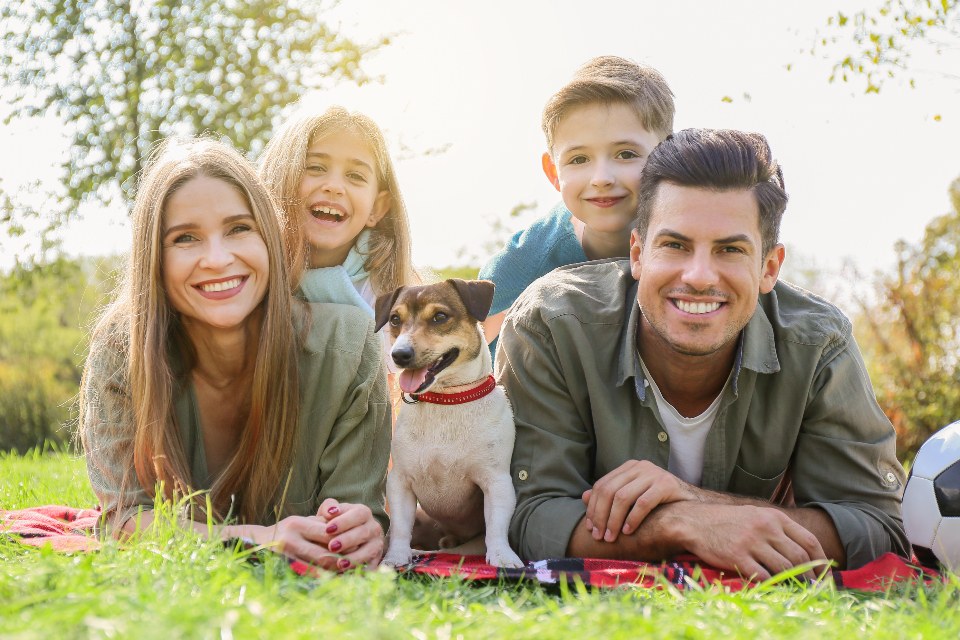 Two adults, two children and a dog together on a picnic blanket outdoors