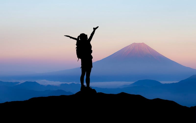 A person silhouetted against a mountain landscape at sunset